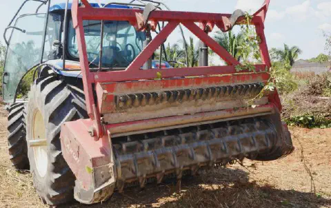 close-up da parte traseira de um trator agrícola de cor azul, ao qual está acoplado um robusto implemento v