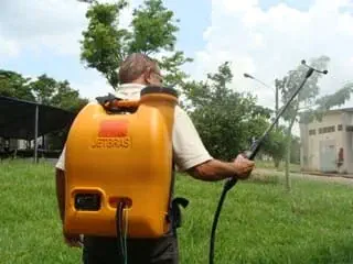 homem, visto de costas, utilizando um pulverizador costal de cor laranja da marca JETBRAS. Ele está em uma