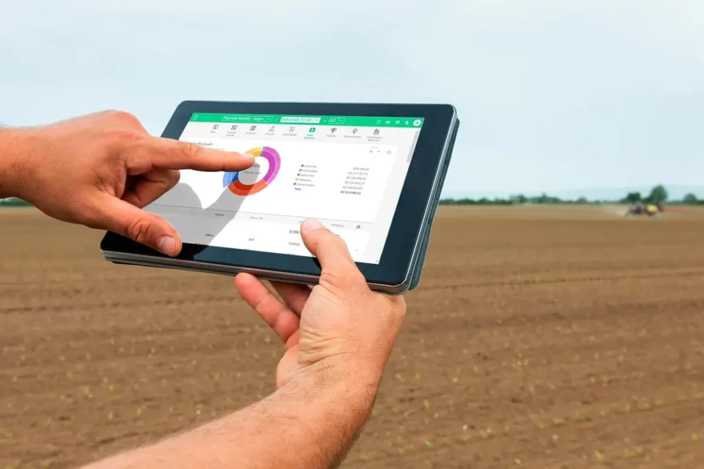 Pessoa segurando um tablet aberto no software da Aegro, mostrando gráficos de gestão financeira em um campo.